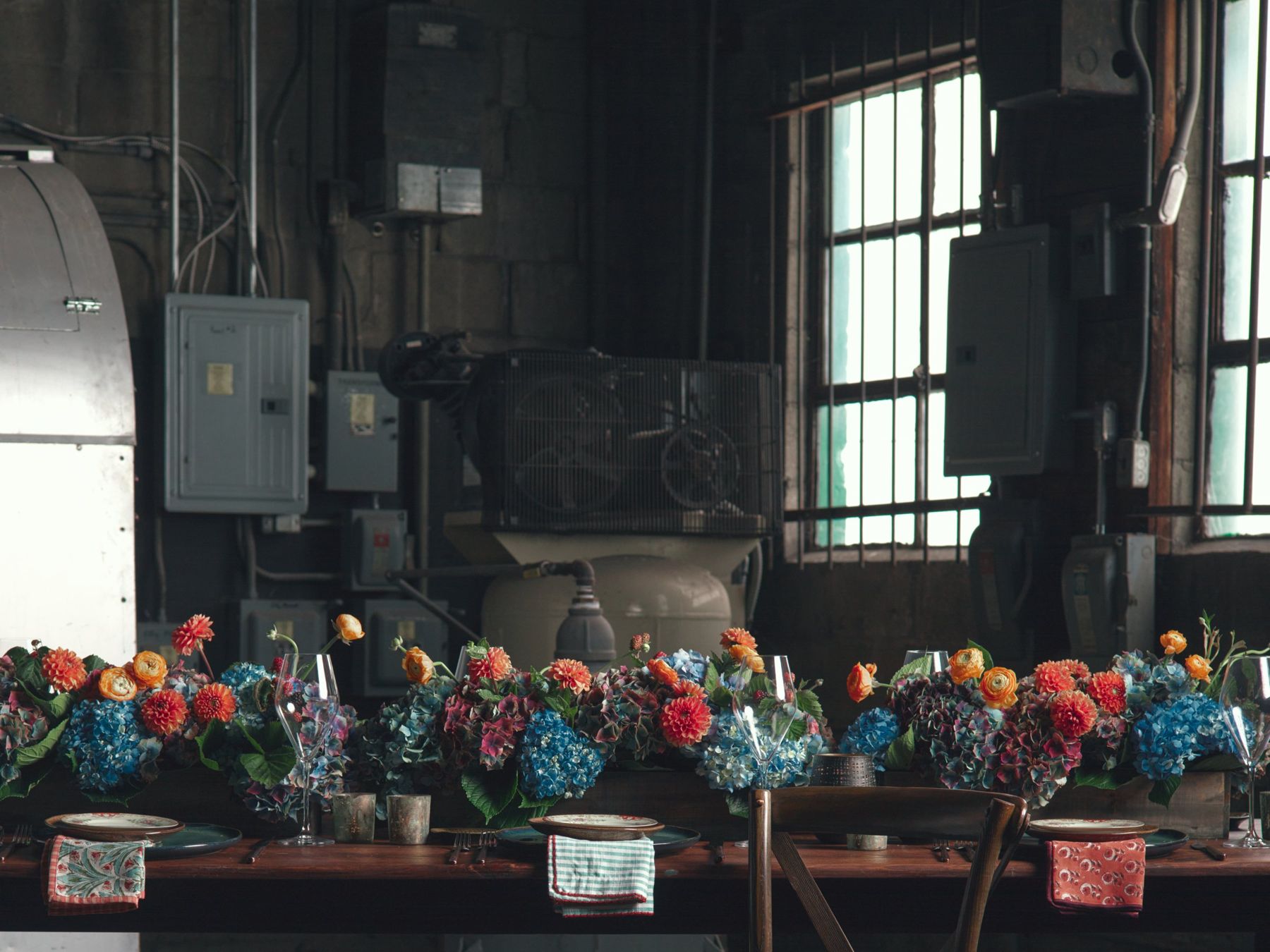 Long industrial-room table lined with colorful floral arrangements