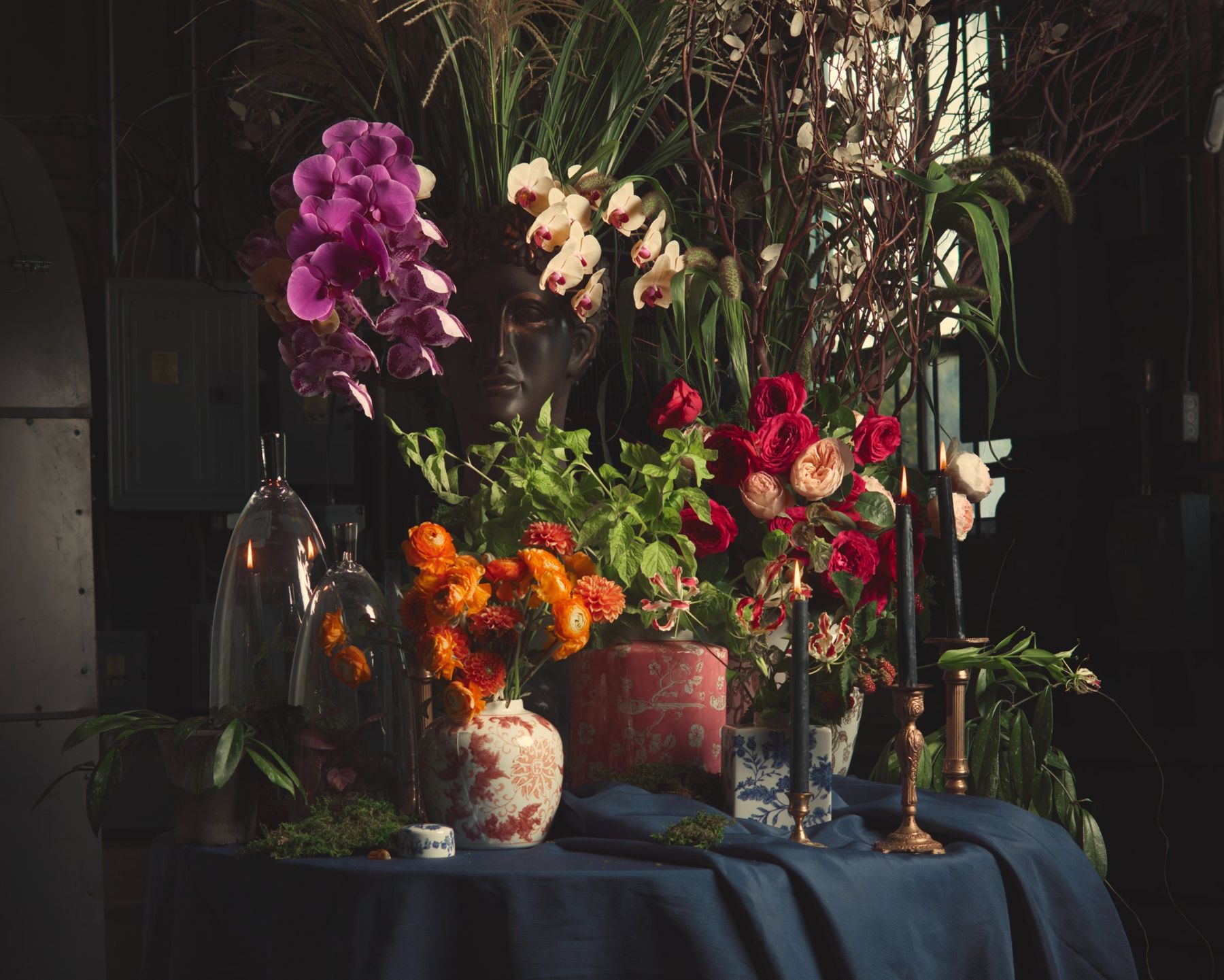 Orchids, roses, and marigolds in vintage vessels on a dark table