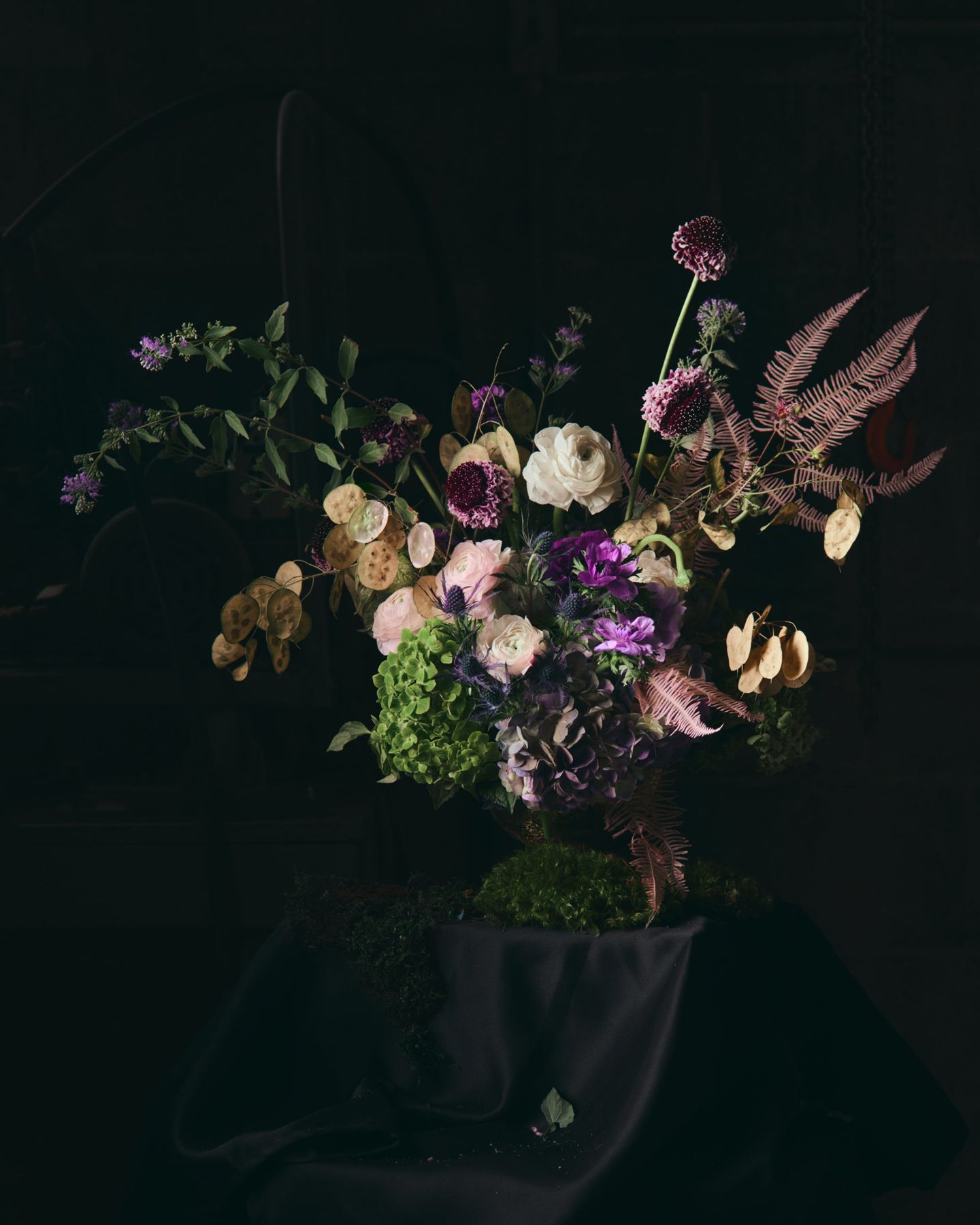 Loose arrangement of pale blooms and purple alliums in a dark studio