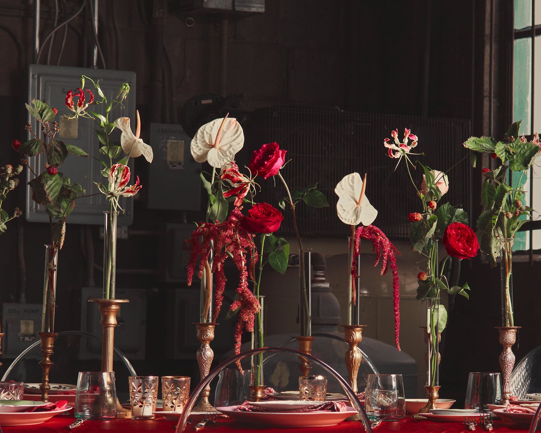 Bud vases of anthuriums and roses along a candlelit table